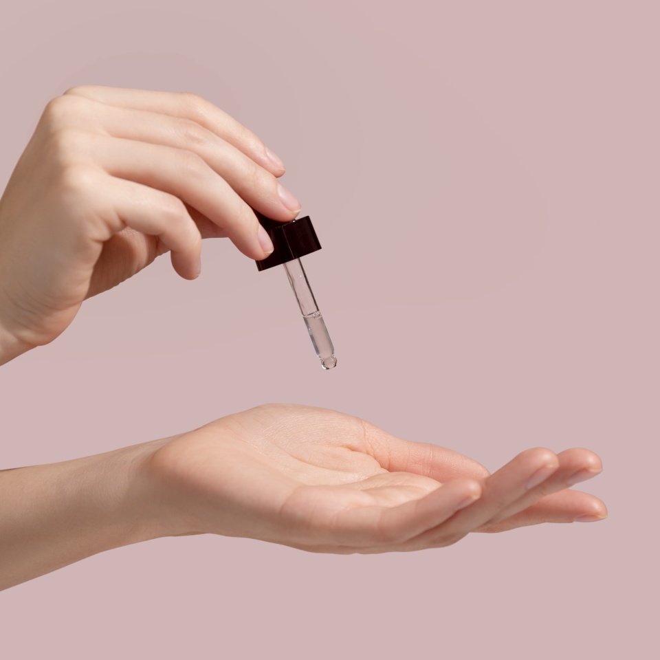 Woman hand holding facial essential oil or serum packaging on pink background. Beauty cosmetic product for skincare concept. Mockup. High quality photo