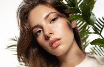 Beautiful woman with perfect skin and natural make-up holding tropical leaves
